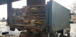 A full construction dumpster packed with broken drywall and wood debris inside a loading facility.