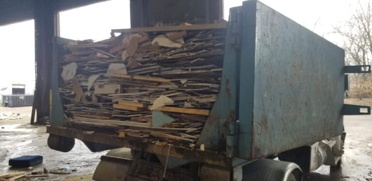 A full construction dumpster packed with broken drywall and wood debris inside a loading facility.