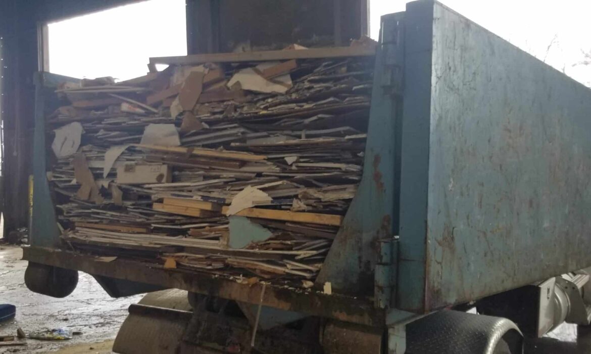 A full construction dumpster packed with broken drywall and wood debris inside a loading facility.